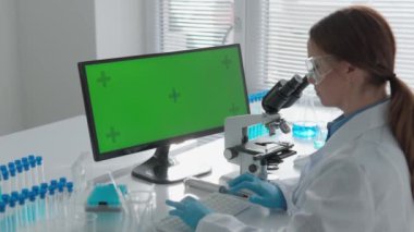 Krom anahtar yeşil ekran. Bilim adamının tıp ve kimya alanında araştırma yaptığı bir laboratuvar. Mikroskop kullanarak biyolojik yapıları inceliyor ve bilgisayar kullanıyor.