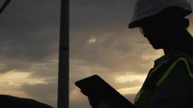 Arka planda güzel bir günbatımı olan rüzgar çiftliğinde çalışan bir mühendisin portresi, gelişim ve çevre sorumluluğu arasındaki ilişkiyi simgeler. Yüksek kalite 4k görüntü