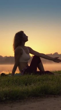 Bir kadın, bir gölün kıyısında yoga pratiğine dalmış, doğaya bağlı hissediyor ve bilincini derinleştiriyor. Ön planda bir güvercin var. Yüksek kalite 4k görüntü