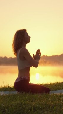 Gölün sakin yüzeyi karşısında bir kadın yoga yapar, doğanın enerjisiyle bir bağ hisseder ve vücudunda ve ruhunda dengeyi korur. Yüksek kalite 4k görüntü