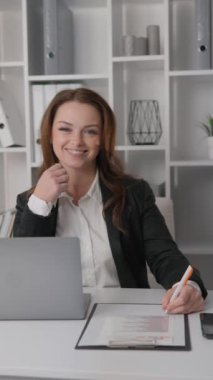 Kameraya bakıp poz veren bu başarılı iş kadını, girişiminin gelişimi üzerinde dikkatle çalışıyor, belgelerin ve laptopun bulunduğu ofis alanındaki bilgisayarına derinden sabitlenmiş.