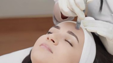 Güzellik kliniğinde yüz mikro tedavi gören bir kadının yakın çekimi. Prosedür beyaz eldivenli bir profesyonel tarafından gerçekleştirilir, deri dokusunu ve görünüşünü iyileştirmeye odaklanır..