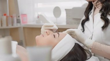 Bir kadın kaplıcada profesyonel yüz bakımı alır. Cilt bakımı uzmanı, cilt sağlığını ve rahatlığını geliştirmek için modern araçlar ve teknikler kullanır..