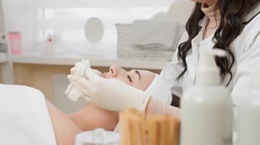 Barışçıl bir spa ortamında, beyaz önlüklü profesyonel bir estetisyen, lekesiz, beyaz bir odada, üst kalite cilt gereçleri kullanarak sakin bir müşteriye yüz bakımı yapar.