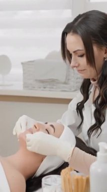 Güzellik kliniğindeki bir kadın estetisyen, iyi aydınlatılmış bir ortamda müşterilerine titiz bir bakım sunar. Cilt bakımına ve sağlık temalarına uygundur. Temizlik ve profesyonelliğe odaklanır.