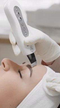 Bir güzellik teknisyeni ultrasonik temizleyici kullanarak yüz bakımı yapıyor. Yakın çekim sahnesi, cihazın cilt bakımını geliştirmek ve cilt bakımını iyileştirmek için ne kadar hassas olduğunu gösteriyor..