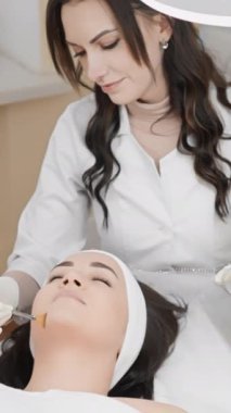 Profesyonel bir kozmetolog, modern bir klinik ortamında gevşemiş bir müşteriye detaylı bir yüz prosedürü uygular. Yakın çekim çerçeveleri cilt bakımı sırasında hassasiyet ve bakımı vurgular.