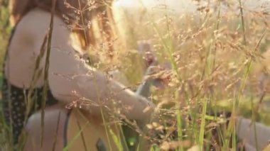 Bir video, doğada huzurlu bir çayırda gitar çalan bir kızla huzurlu bir anı yakalar. Sıcak ortam, sakin atmosferi güçlendirir ve güzel ve uyumlu bir manzara yaratır.