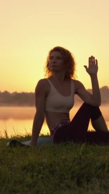 Bir gölün kıyısında yoga yapan, doğanın huzur ve güzelliğinin tadını çıkaran hareketlerindeki güç ve sükuneti yansıtan bir kadının portresi. Yüksek kalite 4k görüntü