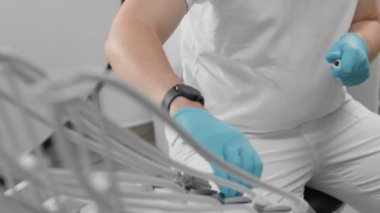 Dişçi rutin bir muayene yapıyor. Tıbbi uzman koruyucu eldiven takıyor ve klinik ortamında gelişmiş diş ekipmanları kullanıyor. Hasta bakımı ve hijyene odaklanmış..