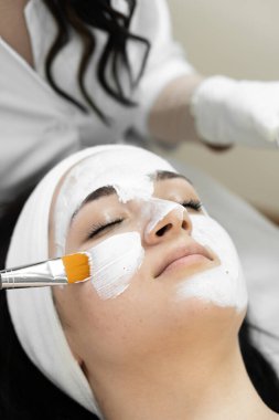 Bir kadın, beyaz kilden bir maskeyle, bir profesyonel tarafından uygulanan huzurlu bir spa seansına katılırken, huzurlu bir ortam deneyimi yaşayın. Rahatlayın ve rahatlatıcı güzellik tedavileriyle gençleşin.