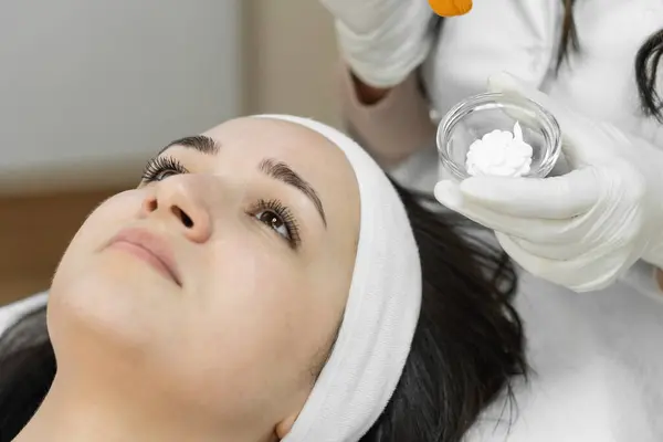 stock image A woman receives a professional facial mask application at a beauty clinic. The skincare specialist prepares to apply the treatment, focusing on enhancing her skins health and appearance.