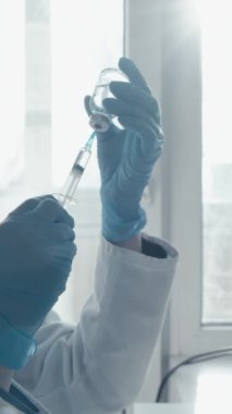 Koruyucu giysiler giyen bir bilim adamı modern bir laboratuvarda araştırma yapıyor. Arkasındaki ekranda veri grafikleri gösterilirken küçük bir şişeye numune enjekte etmeye hazırlanıyor. Eylem konusunda uzman.