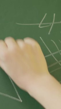 Bir eğitimci, arkasından bakıldığında, yeşil bir karatahtaya matematiksel formüller yazar. Resim dizisi, bir sınıf ortamında öğretim ve matematiksel kavramları açıklama eylemini yakalar..