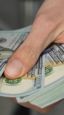Bir resim, Amerikan para biriminin unsurları ile finansal istikrar ve refahı sembolize eden, zenginlik ve kaynakları temsil eden, eller tarafından düzenlenmiş yüz dolarlık banknotları gösteriyor.