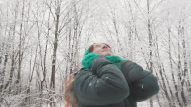 Sakin bir kış manzarasında, rahat yeşil atkı ve sıcak ceketli bir kadın gülümser ve karlı ağaçların arasında sakin orman manzarasını kucaklar, soğuk havada neşe bulur.