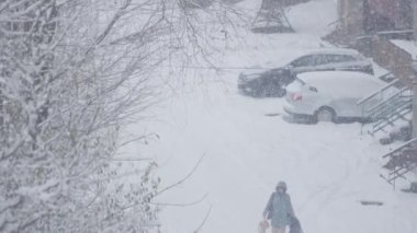 Şiddetli kar yağışı olan şiddetli bir kar fırtınasını tasvir eden bir kış sahnesi. Banliyö yerleşim bölgesinde arabaların üstü karla kaplıyken, yoğun karda yalnız bir insan yürüyor..