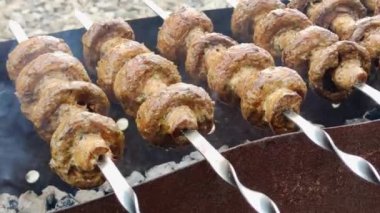 Metal çubukların mangal kömürü üzerinde şişlenmiş mantarların detaylı görüntüsü. Bu iştah açıcı barbekü mantarları açık hava toplantıları için mükemmeldir. Lezzetli ve dumanlı bir lezzet sunar..