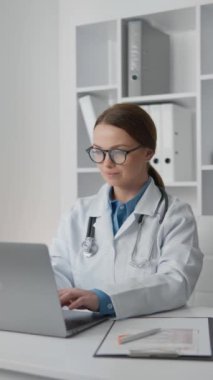 Beyaz önlüklü, gözlüklü, modern bir muayenehanede dizüstü bilgisayarda çalışan kendini işine adamış bir kadın doktor. Hasta bakımını idari görevlerle dengelemek üzere işine odaklanmış durumda..