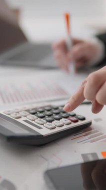 Kesin finansal hesaplamalar ve analizler için hesap makinesi kullanan bir profesyonelin ayrıntılı görüntüsü. Belgeler ve dizüstü bilgisayarların yer aldığı belgede, odaklanmış bir iş ortamının ortamı vurgulanıyor.