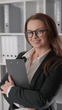 Gösterişli, iyi giyimli bir ofiste, kendine güvenen gözlüklü bir iş kadını başarıyı simgeler. Şirket temalı görseller için ideal, bu sahne profesyonelliği ve kararlılığı ifade ediyor