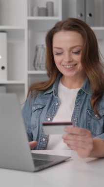 Gülümseyen bir kadın, evde kredi kartı ve laptopuyla online alışveriş yaparken görülüyor. Ekommerce, çevrimiçi alışveriş, dijital ödemeler ve tüketici davranışı hakkında içerik için mükemmel