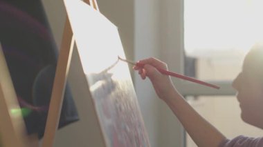 Bir sanatçı, sanatsal tutkularını yansıtan, sehpalarında doğal ışıkla vurgulanan profesyonel bir fırçayla bir tuval üzerinde titizlikle çalışırken, özveri ve beceri sergiliyor.