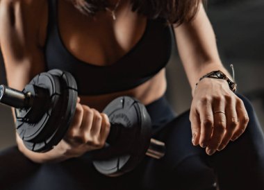 Hareketli giyinmiş kararlı bir kadın modern bir spor salonunda dambılı kaldırıyor, inanılmaz gücünü ve spor yolculuğunu sürdürmeye olan sarsılmaz bağlılığını gösteriyor.