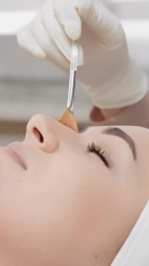 Kozmetik yüz tedavisi gören bir kadının yakın çekimi. Estetisyen burun yakınında bir yüz fırçası kullanır, hassas bir şekilde cilt bakımına odaklanır. Güzellik ve refah temaları için uygun