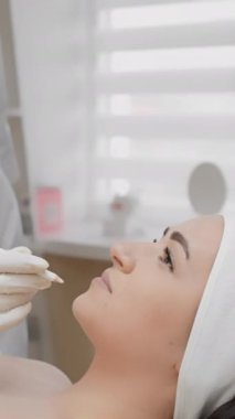 Bir kadın spa ortamında rahatlatıcı bir kozmetik işlemden hoşlanır. Profesyonel, modern cilt bakımı ve hassasiyetini vurgulayan bir yüz tedavisi uygularken eldiven giyer..