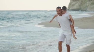 Yürek ısıtan bir sahnede, kendini adamış bir baba keyifle oğlunu pikoresk plajında taşıyor, rahatlatıcı deniz kenarında güzel ve kalıcı anılar yaratıyor keyifli aile tatilleri sırasında.