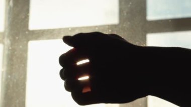 Bir el siluetini gösteren resimler, güneş ışığına karşı bir yıldız patlaması etkisi yaratıyor. Parmakların arasından geçen ışık gölgelerin ve güneş ışığının etkileşimini vurguluyor..