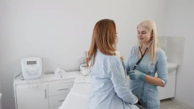 Bir sağlık uzmanı, modern bir klinikte yapılan check-up sırasında hastaların kalp atışlarını dinlemek için steteskop kullanır. Çevre temiz ve hasta bakımı için tasarlanmış..