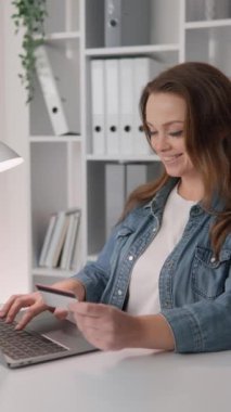 Çağdaş bir ofis ortamında, çalışkan genç bir kadının kredi kartıyla online alışveriş yaptığı, iş yerinde verimli ve profesyonel alışveriş davranışları sergilediği gözlemleniyor.