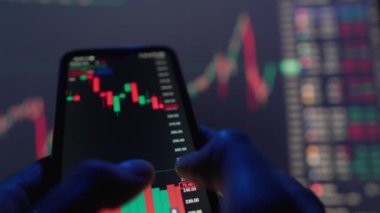 Bir mobil cihazın borsasını analiz eden kişi, şamdan çizelgelerine ve grafiklere odaklanarak, bir piyasa senaryosuna işaret ediyor. Finansal analiz ve ticaret temaları için mükemmel.