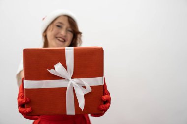 Neşe dolu gözlerle, bir kadın yeni yılı ve Noel 'i kutlamanın sevincini simgeleyen bir hediyeyi elinde tutuyor. Kırmızı arka planda bir kış tatili atmosferi. Yüksek