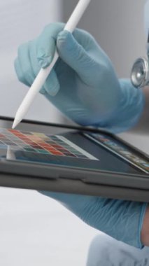 Eldiven ve steteskop giyen bir sağlık uzmanı hasta kayıtları veya tıbbi veri girişi için stili olan dijital tablet kullanır. Bu etkileşim hastane ya da klinik ortamında gerçekleşir.