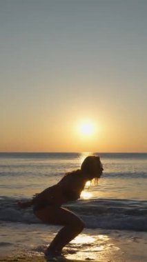 Gün batımında sevinçle sahile atlayan bir kadının çarpıcı silueti, doğanın nefes kesen güzelliğini vurgularken özgürlüğün ve mutluluğun güzel özünü yakalıyor.