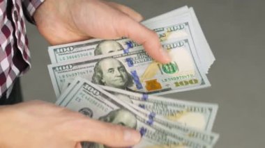Sayısız 100 'lük banknot sayan birinin yakın çekim görüntüleri. Eller yeni banknotları dikkatlice ayırıyor ve Amerikan para biriminin detaylarını gözler önüne seriyor. Finansal ve refah açısından ideal