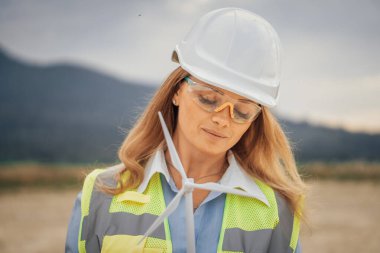 Sert bir şapka ve güvenlik gözlüğü takmış kendini işine adamış bir kadın inşaat işçisi zorlu bir inşaat alanında güç, kararlılık ve profesyonellik gösteriyor.