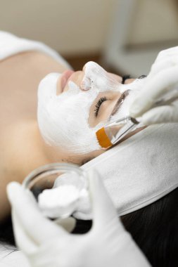 Huzurlu bir ortamda, bir kadın, bir profesyonel tarafından uygulanan krem maskeyle lüks bir spa yüz tedavisi alır. Cildi için rahatlatıcı ve canlandırıcı bir deneyim yaşar.