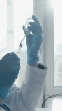 Koruyucu giysiler giyen bir bilim adamı modern bir laboratuvarda araştırma yapıyor. Arkasındaki ekranda veri grafikleri gösterilirken küçük bir şişeye numune enjekte etmeye hazırlanıyor. Eylem konusunda uzman.