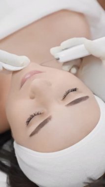 Spa 'da, deneyimli bir estetisyen kadın yüz tedavisi için özel ekipman kullanır, sağlığını destekler ve rahatlama ve lüks bir ortamda cildini tazeler.
