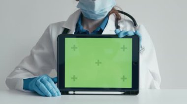 Beyaz önlük, maske ve eldiven giyen bir tıp uzmanı yeşil ekranlı dijital tablet tutuyor. Tıbbi ve sağlık sunumları ve tanıtım içeriği için mükemmel.