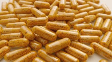 Turuncu kapsüller ve biberli diyet takviyesi. Beyaz arka planda kapsül koleksiyonu, sağlığın ritmine göre dönüyor. Sağlıklı Yaşamın Yolu: İlaç Endüstrisi