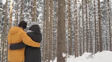 Güzel, sakin, karlı bir ormanda, bir çift kucaklaşır, sıcacık anı kucaklarlar, uzun ağaçlar ve yumuşak kar taneleriyle çevrili, sevgi ve doğanın çekiciliğini gösteren.