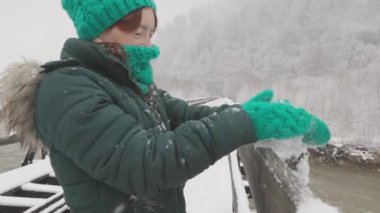 Sıcak kış kıyafetlerini giymiş neşeli bir kadın, sakin kar tanelerinin dingin güzelliğiyle eğlenirken aynı zamanda huzurlu bir kış manzarasında Noel ve Yeni Yıl ruhunu somutlaştırıyor.