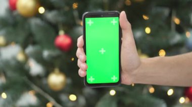 Parlayan bir Noel ağacının önünde neşeli bir akıllı telefon sergileniyor, Noel neşesini, hediye fikirlerini ve sıcak dilekleri paylaşmak için ideal, aileleri yakınlaştırmak ve neşeli anılar yaratmak için.