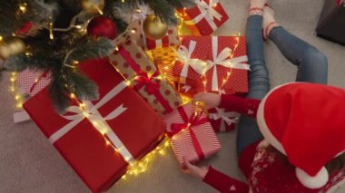 Sarılı kırmızı hediyeler, parlak kurdeleler ve parıldayan ışıklarla dolu canlı bir sahne hayal edin. Bu sezonun neşeli ruhunu ve beraberliğini kutlayan sıcak bir Noel atmosferi yaratıyor.