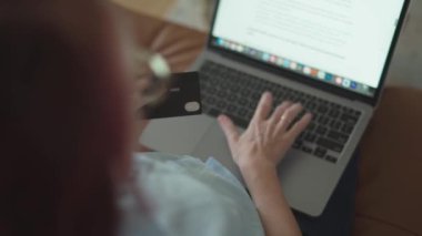 Yakın plan bir dizüstü bilgisayarda, yakınlarda bir kredi kartıyla yazı yazan bir el, çevrimiçi alışveriş ve dijital bankacılığın özünü samimi bir ortamda yakalıyor, modern tüketimcilik kolaylığını gösteriyor